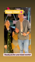 A boy and his mother standing together in an indoor setting, smiling and waving. The man wears a gray cardigan over a white shirt and light blue jeans, while the woman wears a black blazer over a dark green dress with small gold motifs.