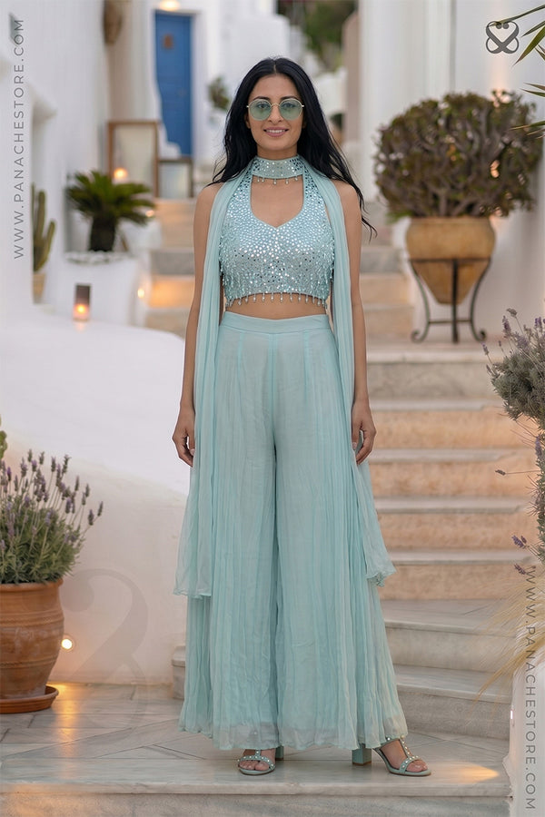 Woman in a light blue outfit standing on a staircase with plants and decor in the background.