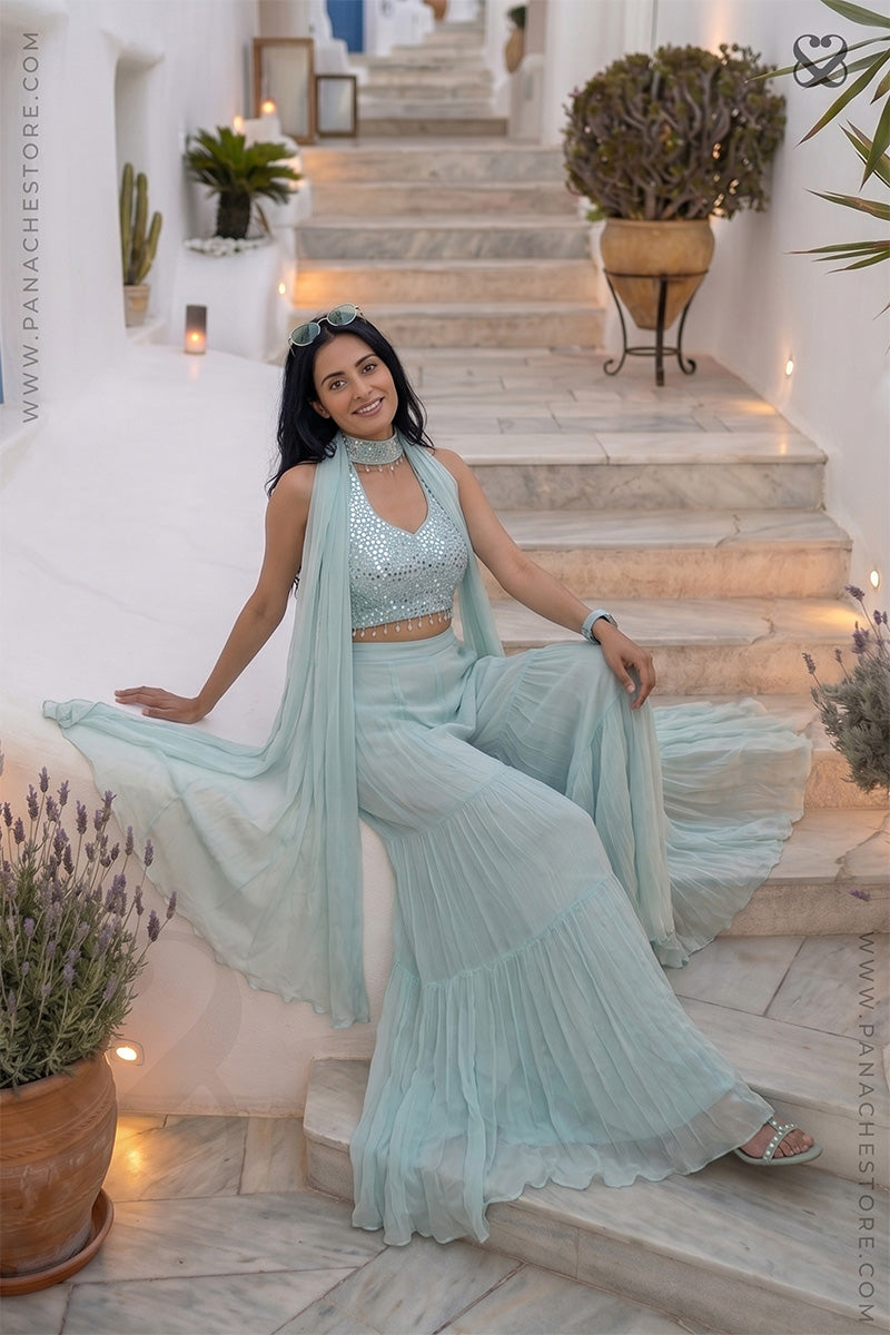 Woman in a light blue traditional outfit sitting on stone steps with decorative plants around.