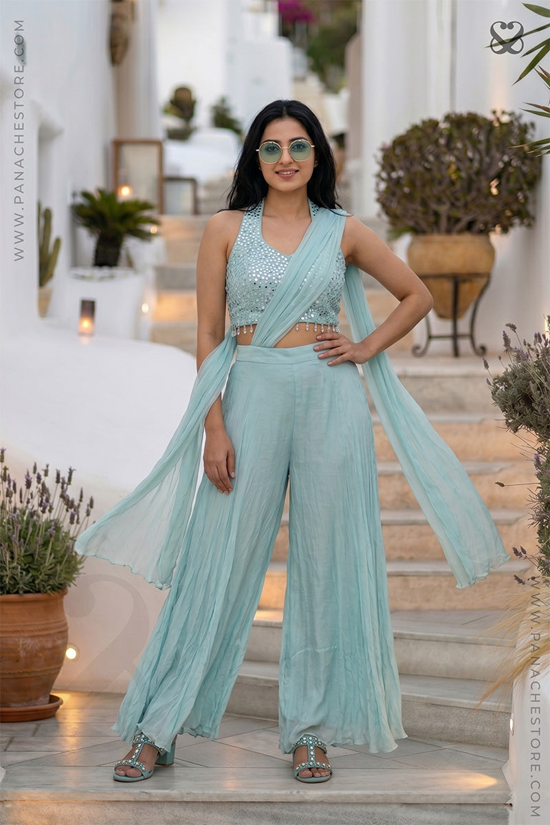 Woman in a light blue traditional outfit standing on a staircase with plants around.