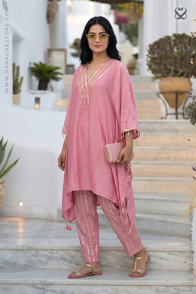 Woman in a pink kaftan top with zari neckline and zari strip pants standing on steps