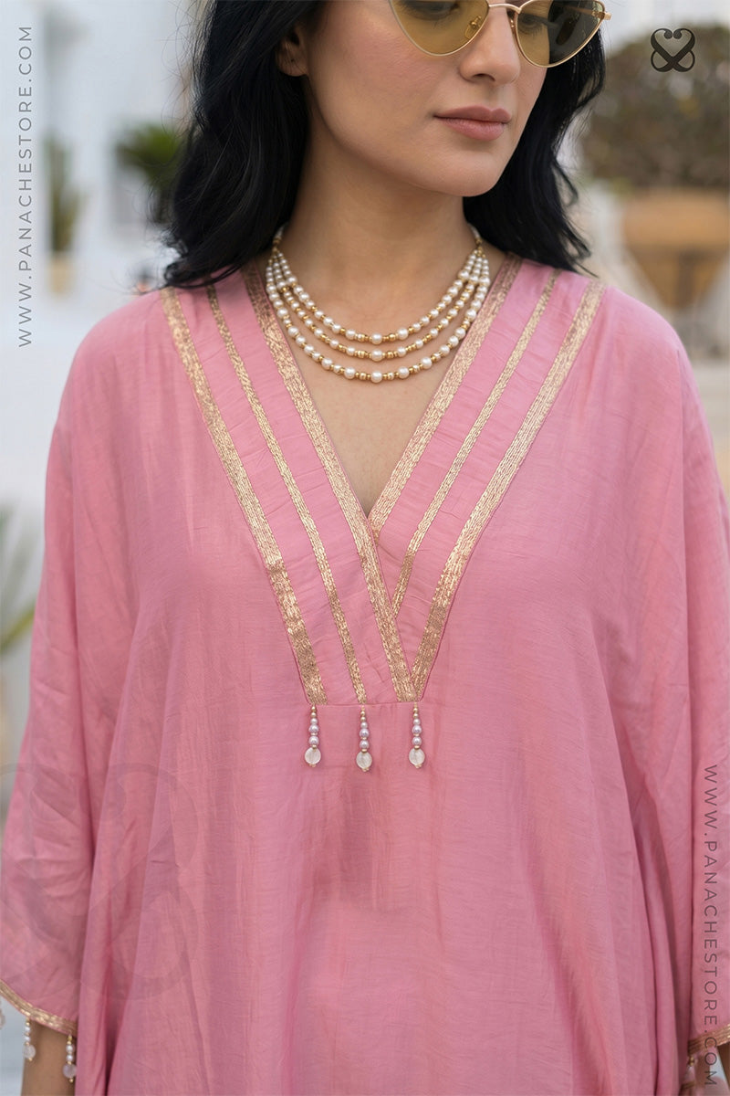 Woman wearing a pink kaftan outfit with gold zari strip neckline and pearl necklaces.