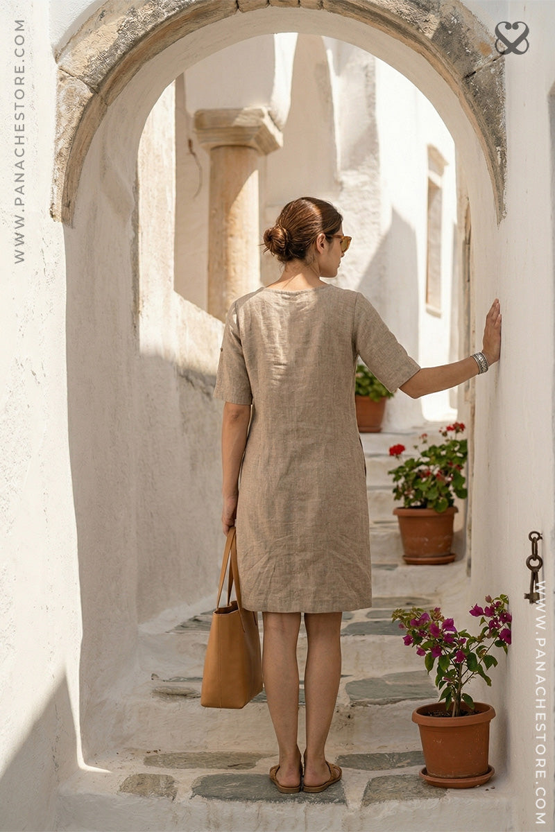 Woman in a beige dress standing in an archway with plants and flowers around.
