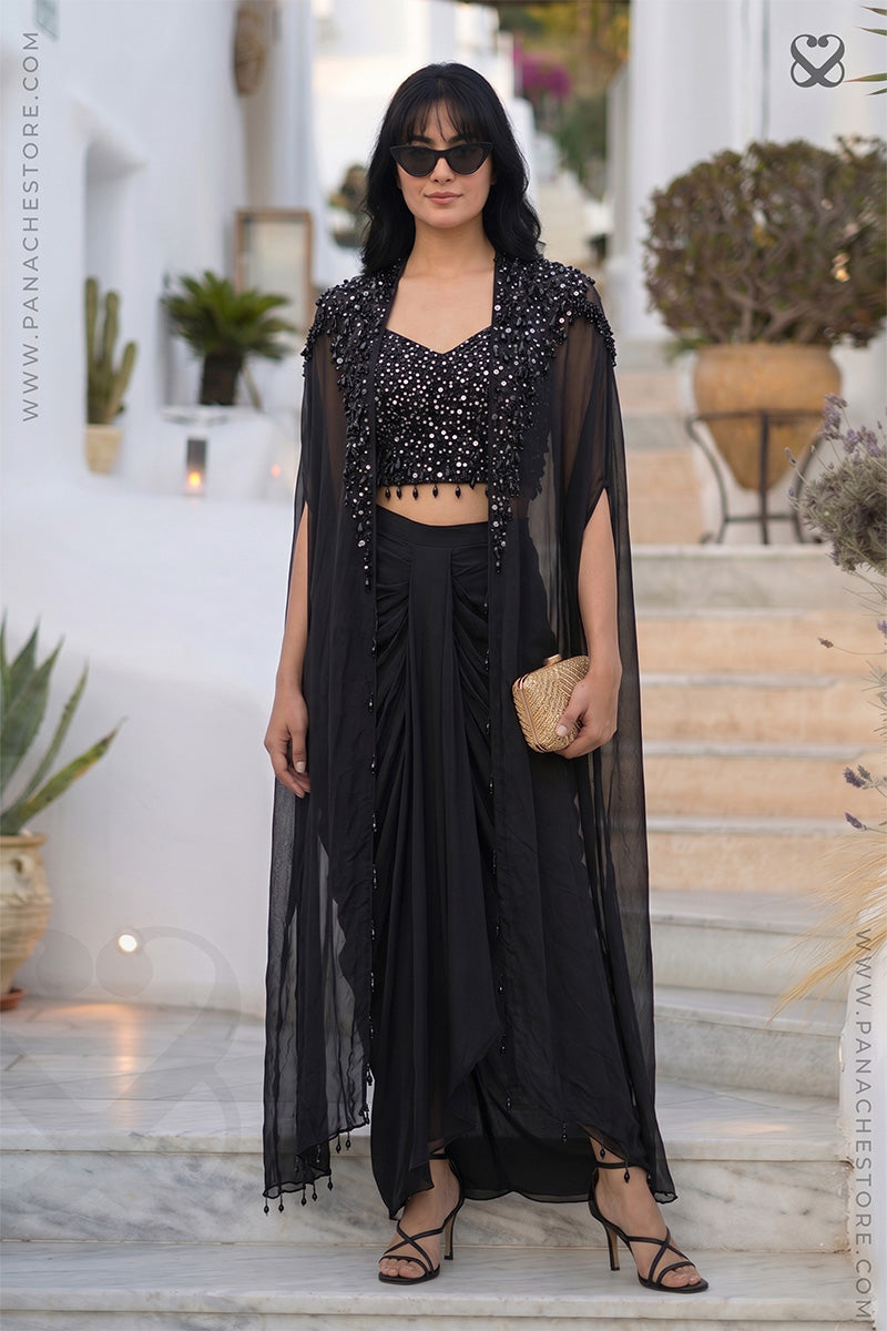 Woman in a designer black color embellished shrug cape and sequin crop top with black skirt standing on outfoor steps