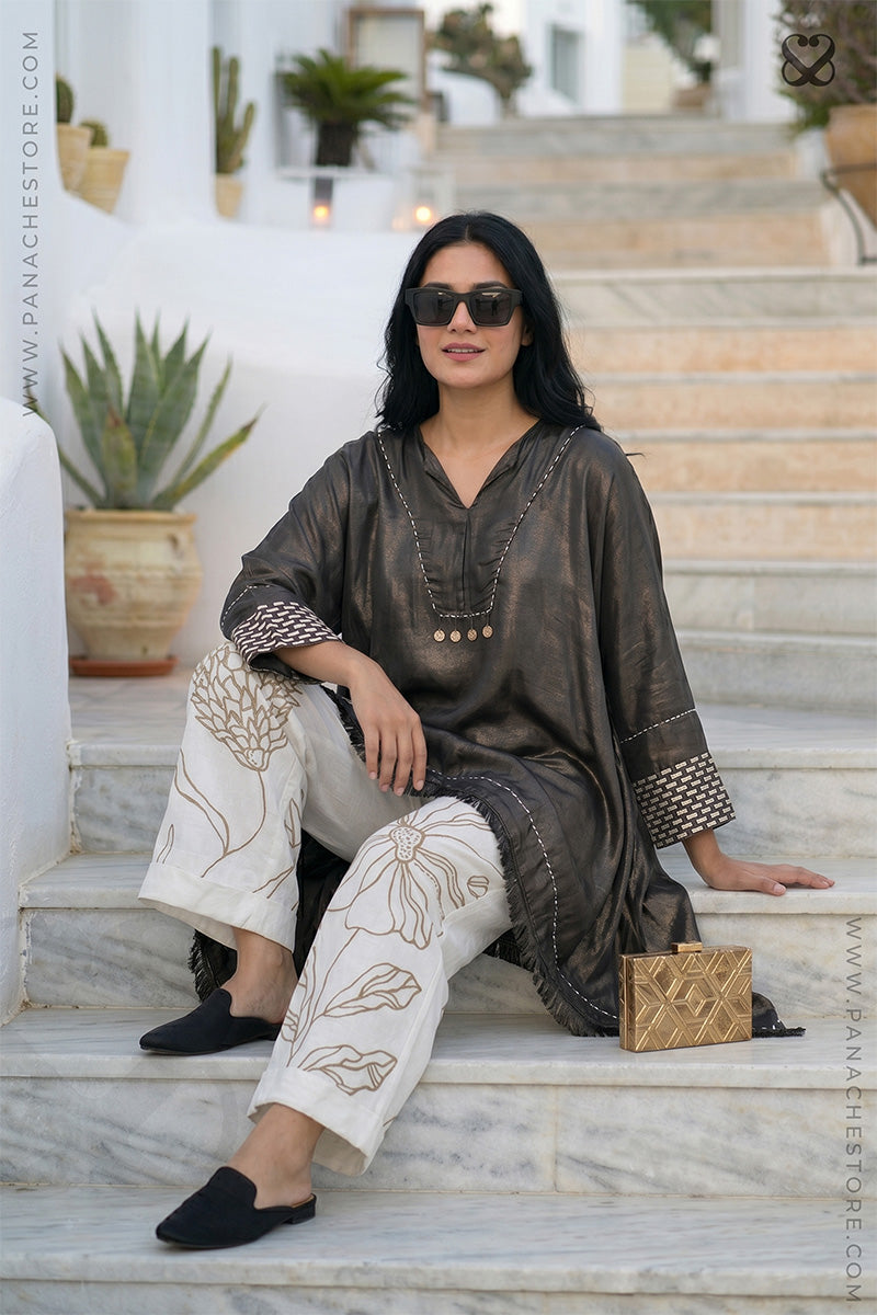 Woman sitting on steps wearing a dark long-sleeve top and light pants with a brand logo in the corner.