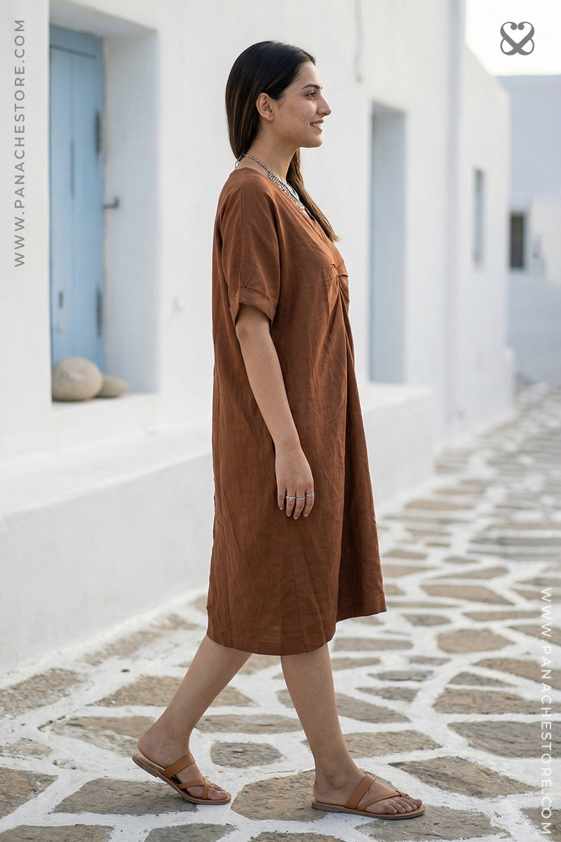 Woman in a brown dress walking on a stone pavement in a sunlit street.