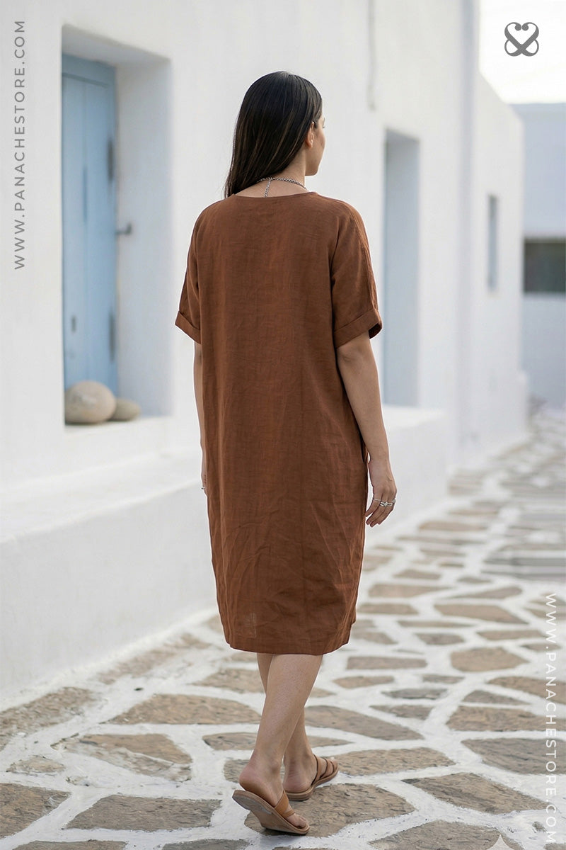 Woman wearing a brown dress walking on a stone pavement with white walls in the background.