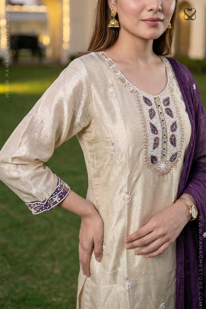 Woman wearing a cream embroidered kurta with a purple dupatta against a blurred outdoor background