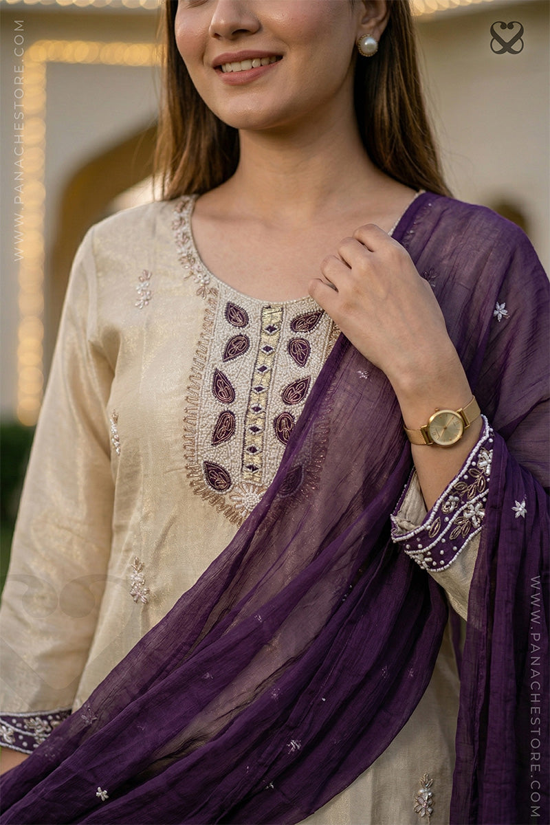 Woman wearing a beige embroidered top with a purple dupatta, smiling outdoors.