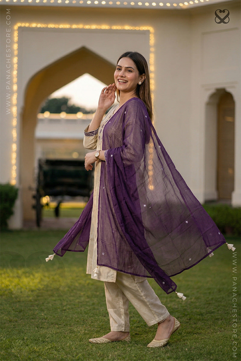 Woman in cream white slawar suit set with purple dupatta standing on grass