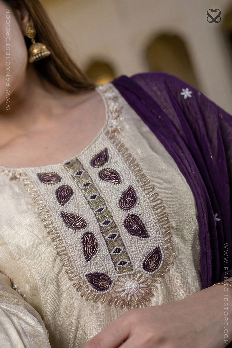 Close-up of a person wearing a cream-colored outfit with intricate purple and green embroidery, paired with a purple dupatta.