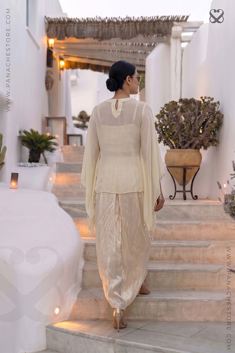 Woman in a cream color traditional kaftan and dhoti style skirt standing backpose on steps