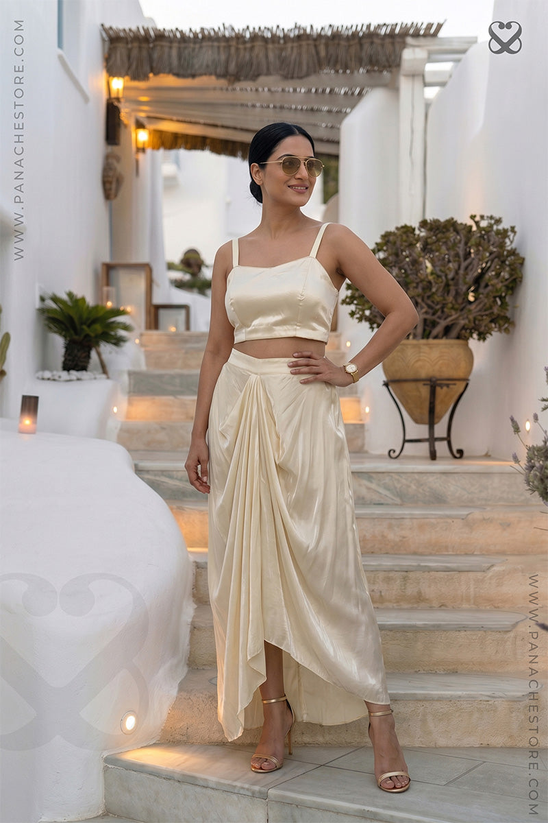 Woman in a cream color specdy blouse and dhoti style skirt standing in an outdoor setting.