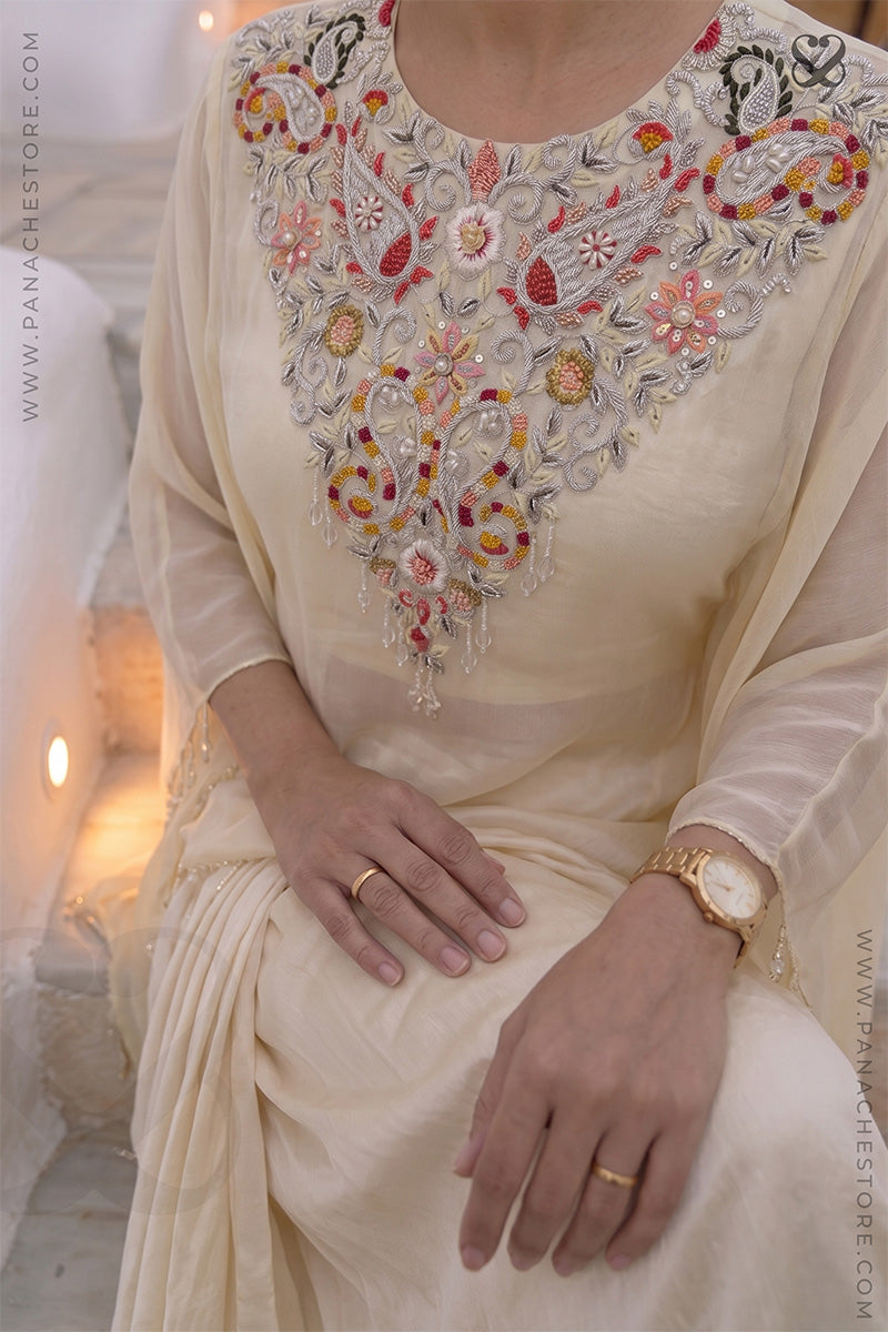 closeup shot of a woman in a cream color traditional kaftan with desiger embellished neckline and dhoti style skirt standing in an outdoor setting.