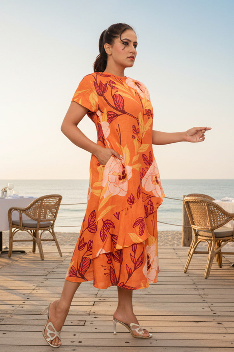Woman in an orange floral dress standing on a wooden deck by the sea.