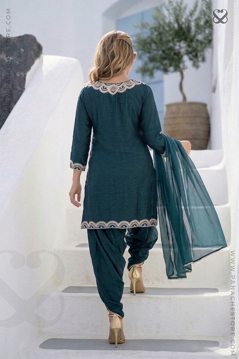 Woman in a teal traditional outfit with white embroidery walking on a white staircase.
