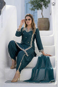 Woman in a deep teal salwar suit set traditional outfit with gold accents sitting on white steps.