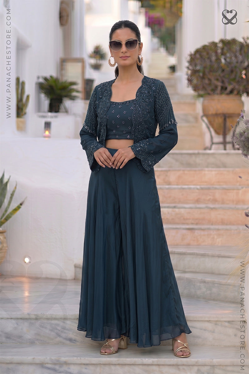 Woman wearing a designer deep peacock teal heavy embellished shrug top with matching skirt sitting on steps