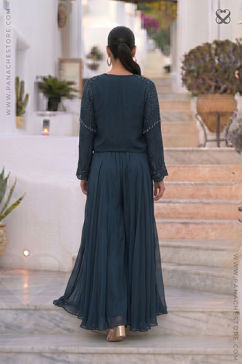 Woman in a dark teal green dress standing on a staircase with decorative plants in the background.