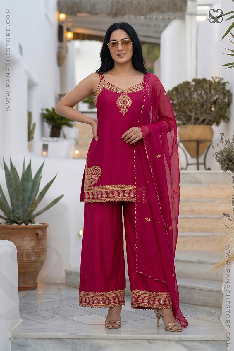 Woman in a pink traditional sleeveless kurti top and plazo pants both with gold embroidery embellishments standing in an outdoor setting.