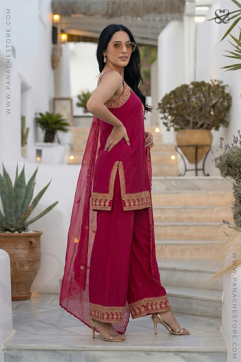 Woman in a pink traditional sleeveless kurti top and plazo pants both with gold embroidery embellishments standing in an outdoor setting.