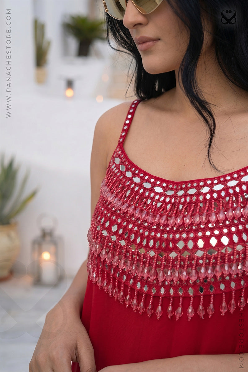 Woman wearing a red crochet top with fringe details in an outdoor setting.