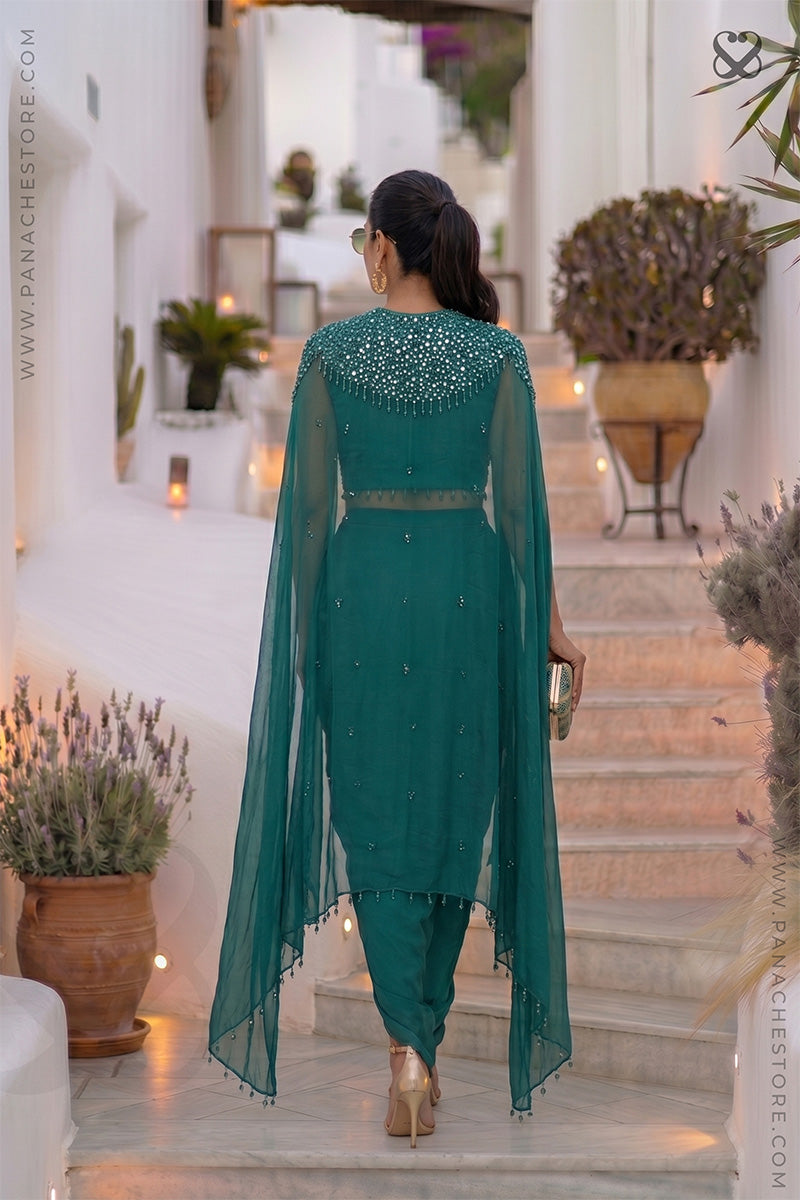 Woman wearing a designer teal sapphire green embellished shrug & blouse top with matching skirt standing back on steps