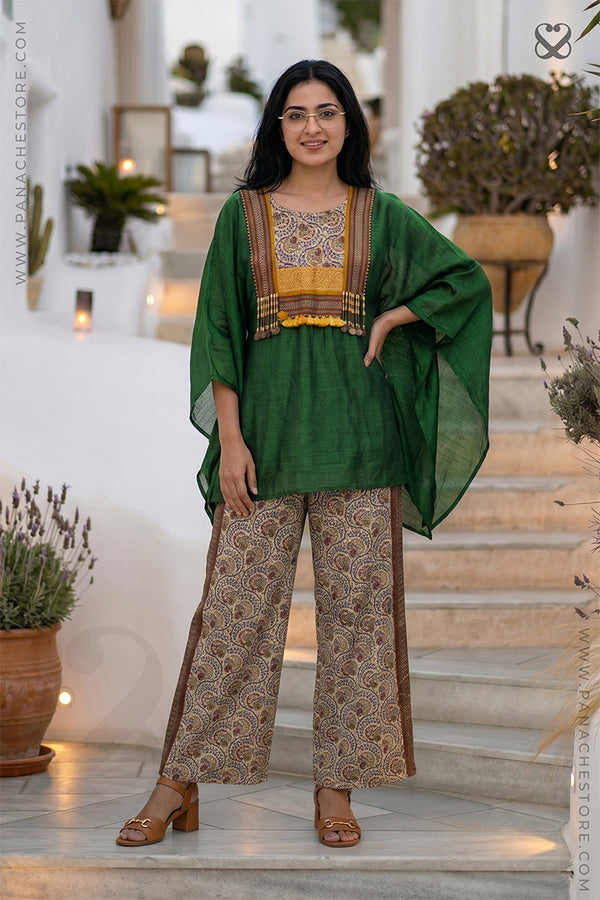 Woman in a green and beige Kaftan and printed beige pant outfit standing on steps