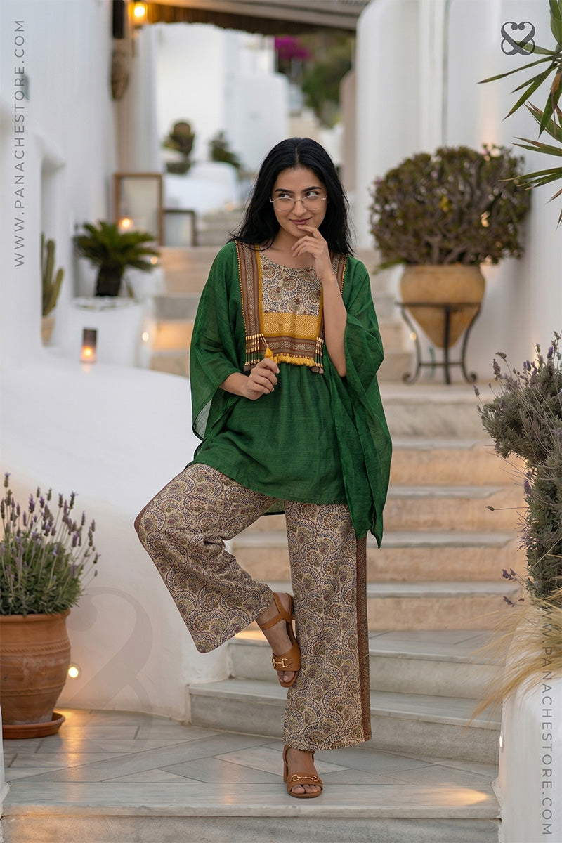 Woman in a green and beige Kaftan and printed beige pant outfit standing on steps