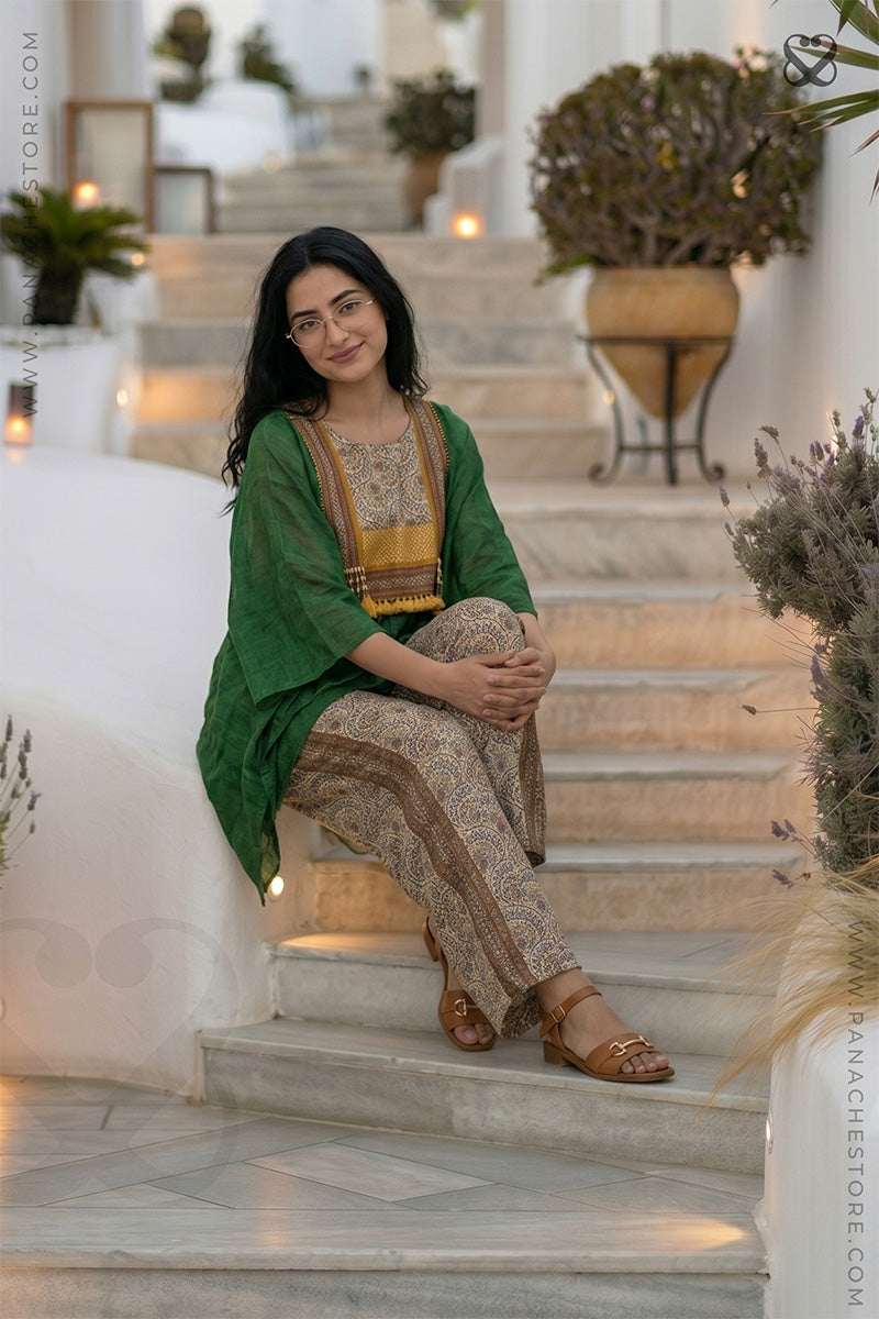 Woman in a green and beige Kaftan and printed beige pant outfit sitting on steps