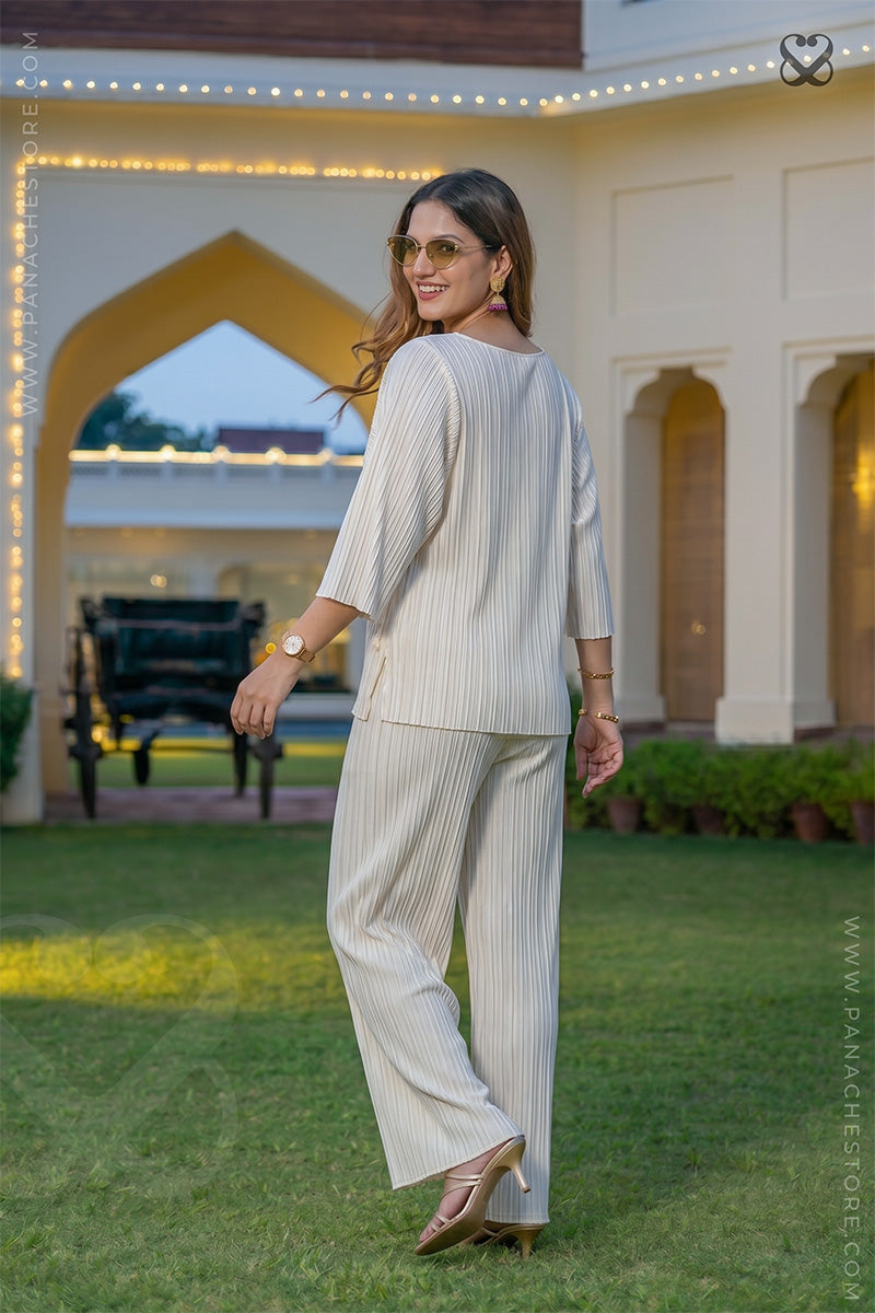 Woman in a white top-pant outfit standing in garden posing back