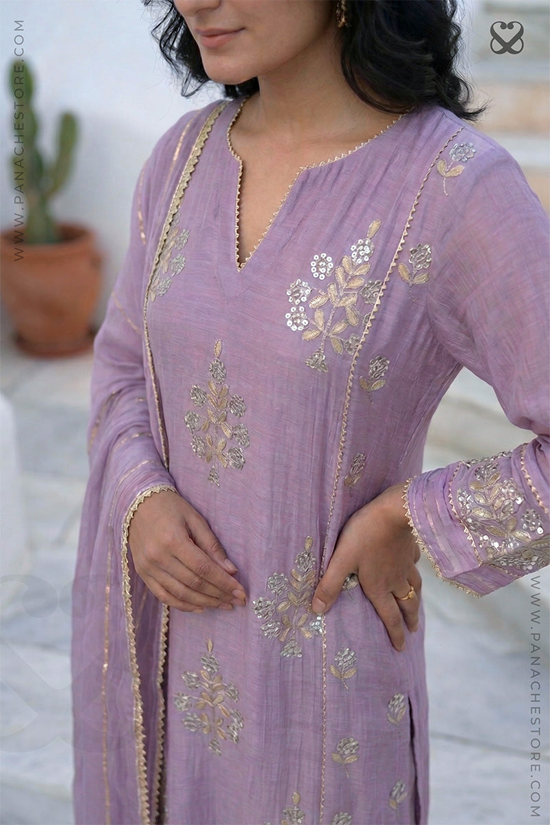 Woman wearing a lavender embroidered outfit with a blurred background