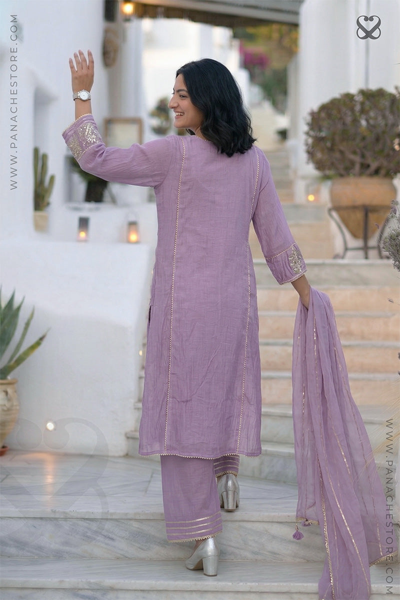 Woman in a lavender salwar suit dupatta standing on steps outdoors.