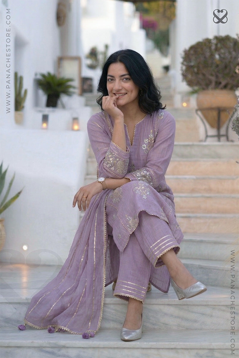 women in a lavender kurti salwar suit with embellishments and matching pant sitting on steps