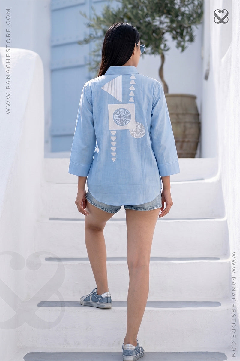 Woman in light sky blue shirt with geometrical embroidery on back moving up on stairs