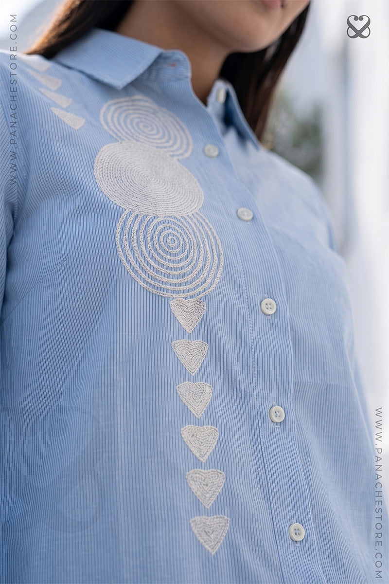 Blue shirt with white geometrical embroidery details on a blurred background