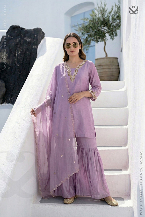 Woman wearing a lavender salwar suit set and dupatta with gold embellishments standing on steps