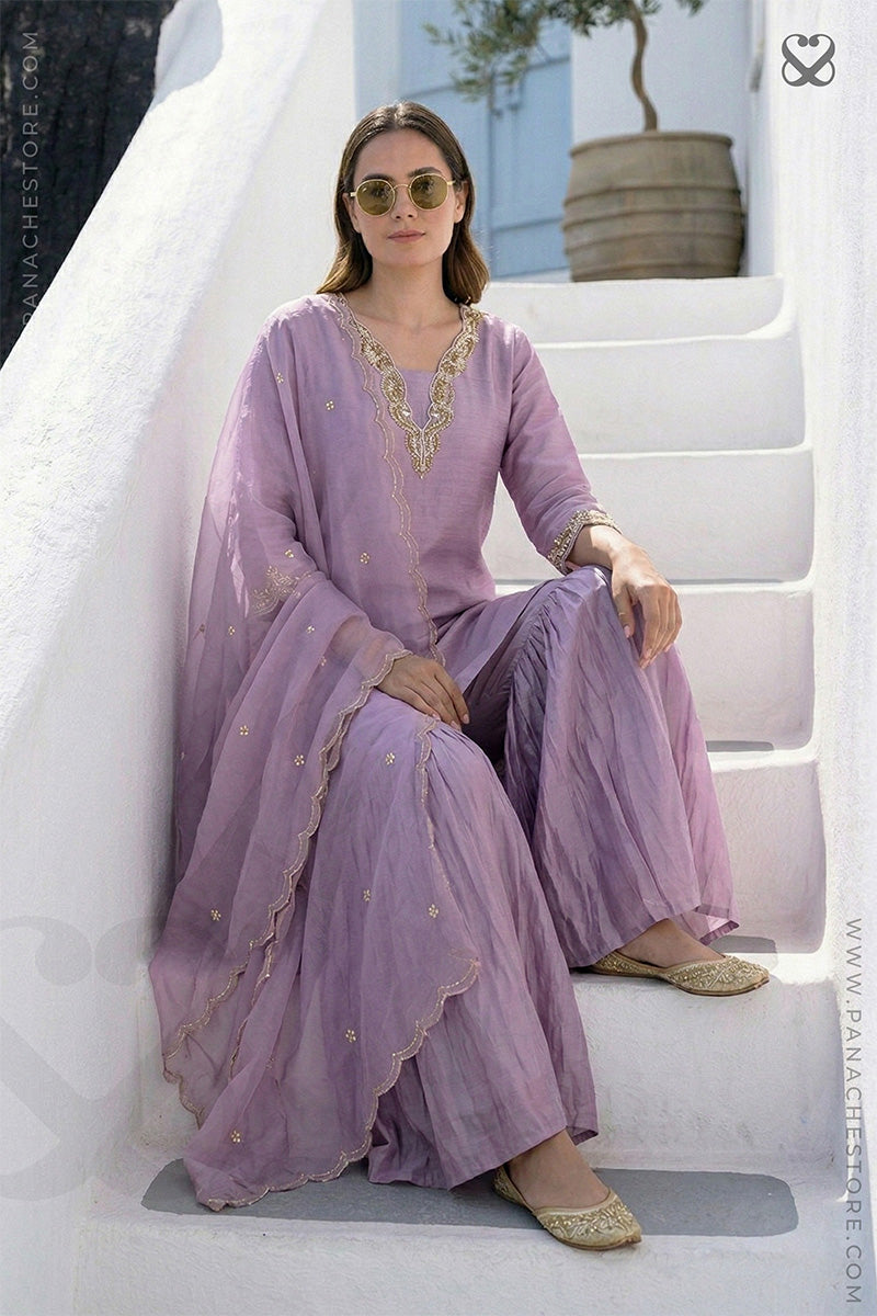 Woman wearing a lavender salwar suit set and dupatta with gold embellishments sitting on steps