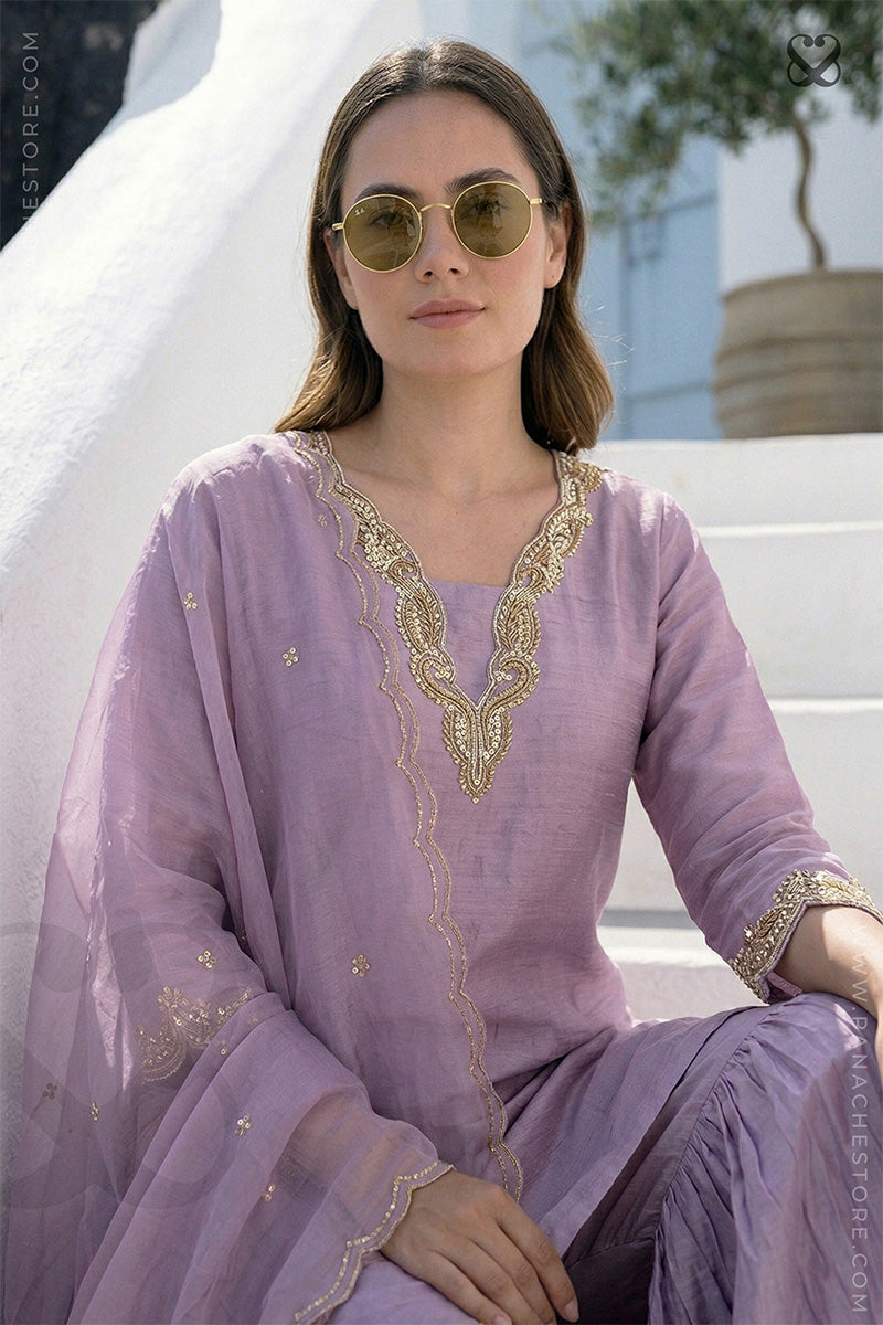 Woman wearing a lavender salwar suit set and dupatta with gold embellishments sitting on steps