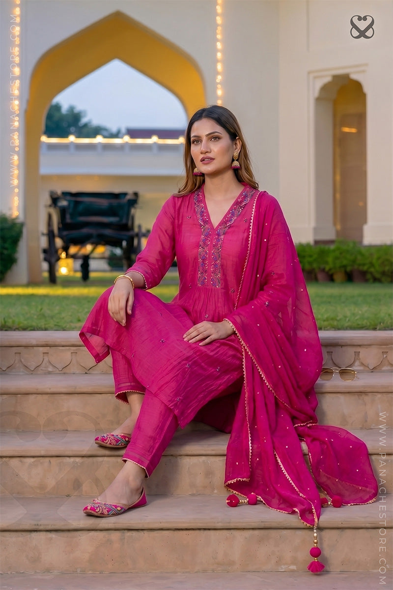 Woman in a deep pink salwar suit set and organza dupatta sitting on steps