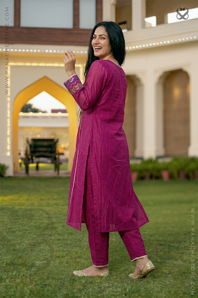 Woman in a magenta traditional outfit standing on grass with a building in the background