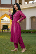 Woman in a magenta traditional outfit standing outdoors with a building and greenery in the background.