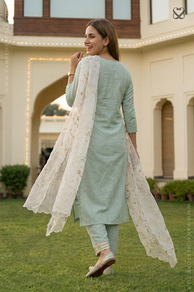 Woman in a light mint green salwar suit set and organza floral dupatta walkin back in a garden