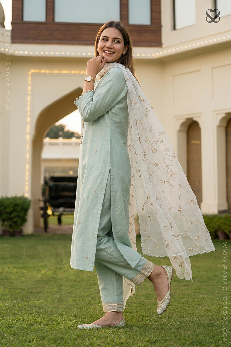 Woman in a light mint green salwar suit set and organza floral dupatta standing in a garden