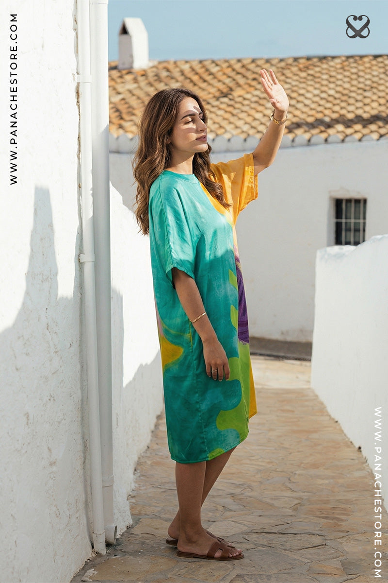 Woman in a colorful dress standing on a sunlit rooftop with white walls and a blue sky.