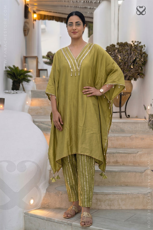 Woman in an olive green Kaftan and zari strip orange pant outfit standing on steps