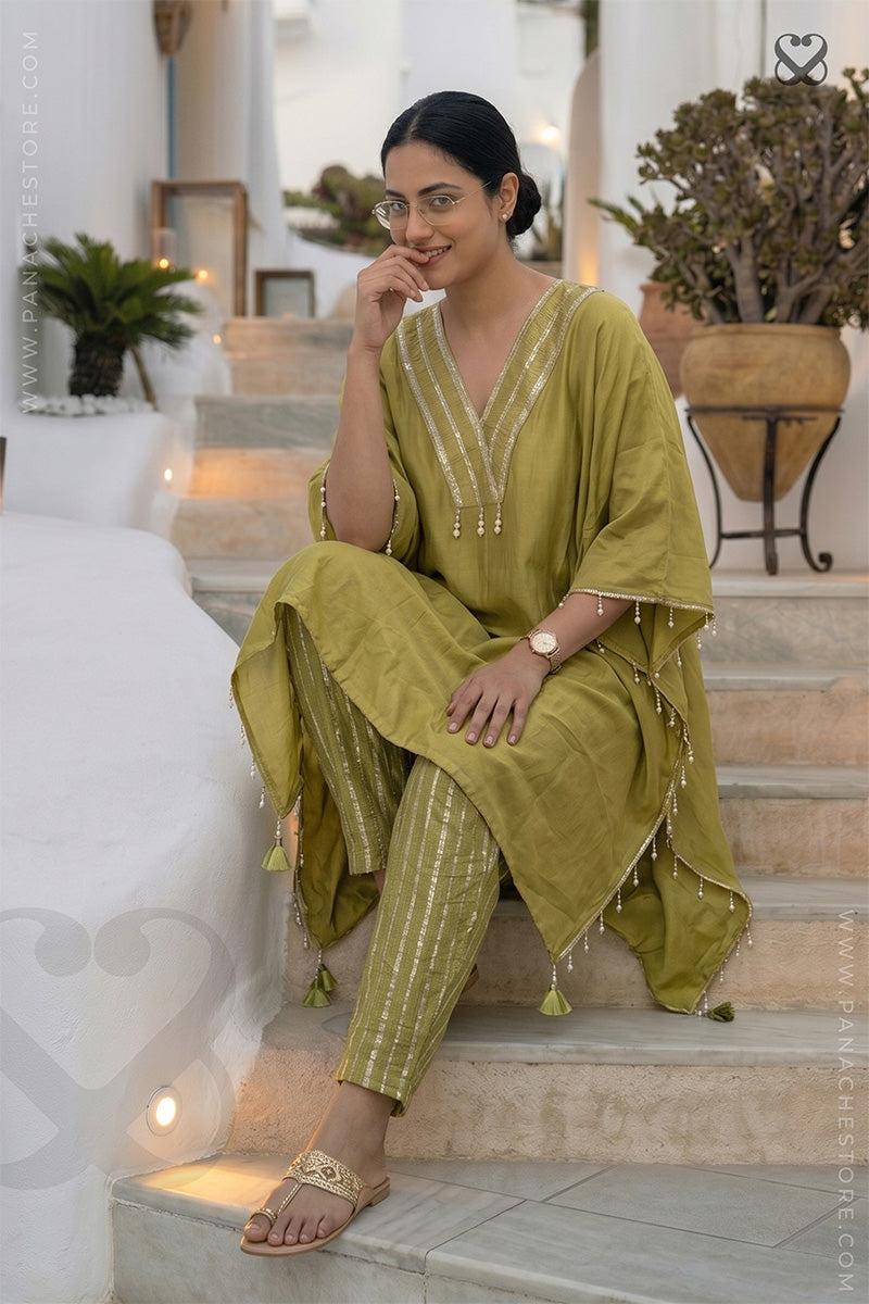 Woman in an olive green Kaftan and zari strip orange pant outfit sitting on steps