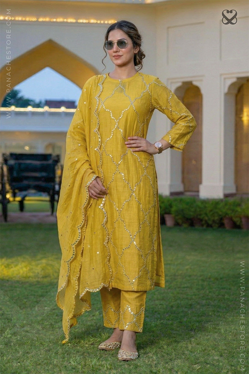 Woman in a designer yellow salwar suit set with mirror work and matching dupatta standing in a garden