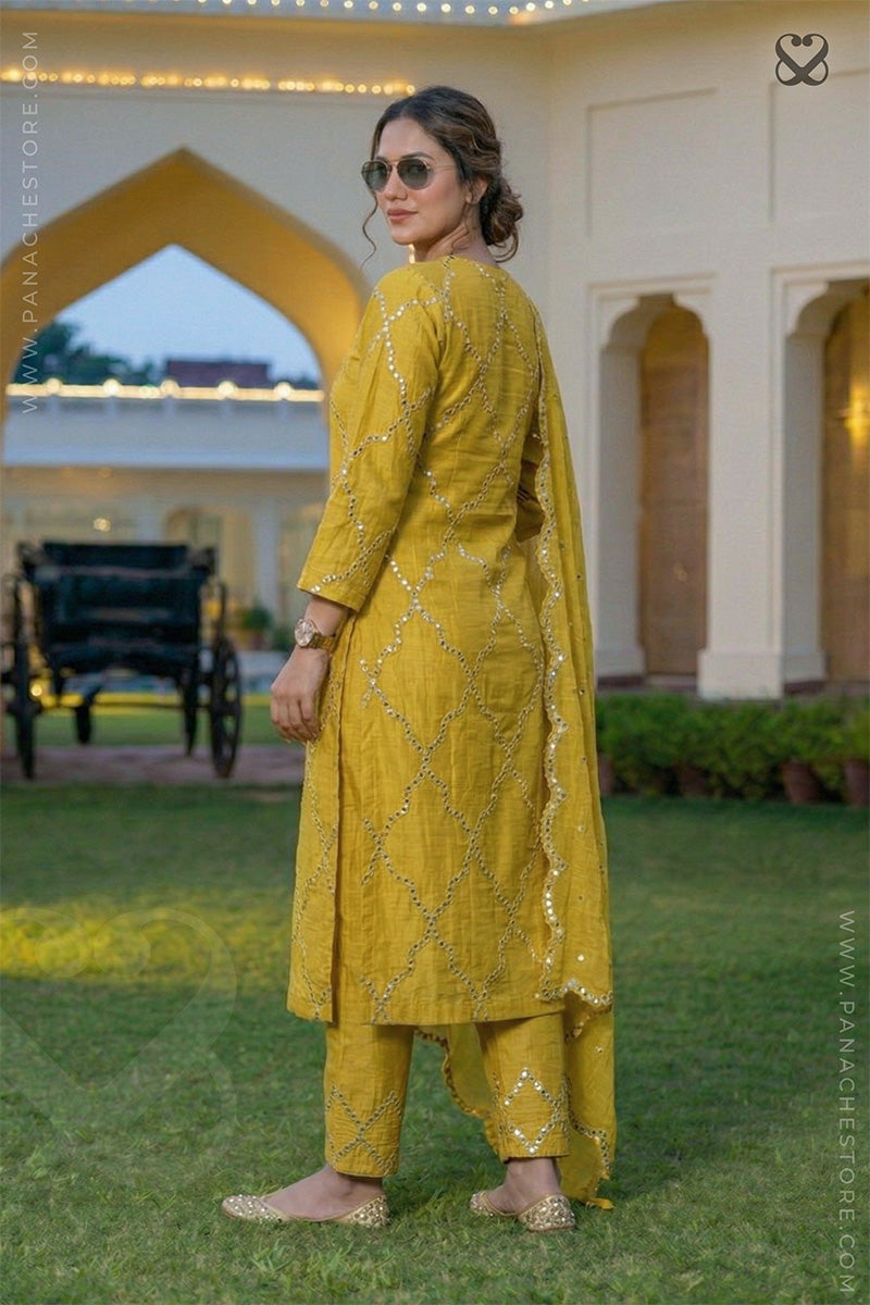 Woman in a yellow designer suit set with mirror work and matching dupatta back profile pose in a garden