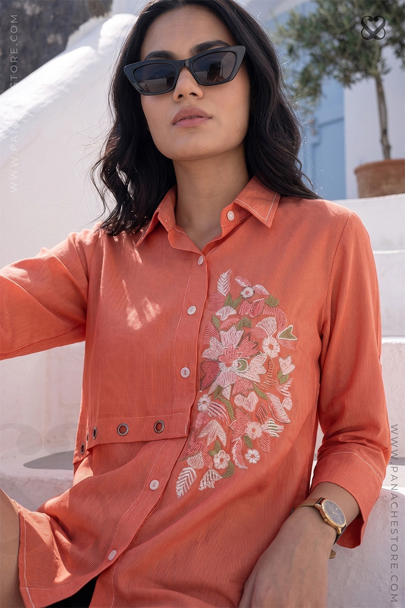 Woman wearing an orange floral embroidered shirt with sunglasses outdoors.